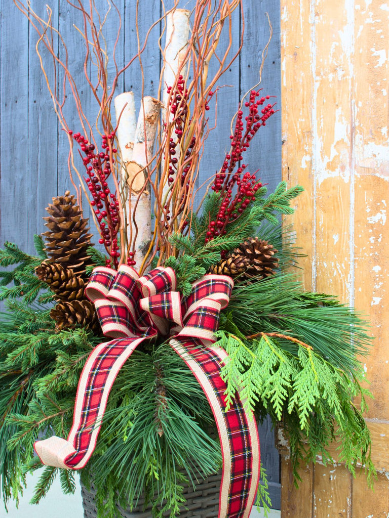 Decorative Christmas arrangement with greenery, berries, pinecones, and a plaid ribbon against a wooden background.