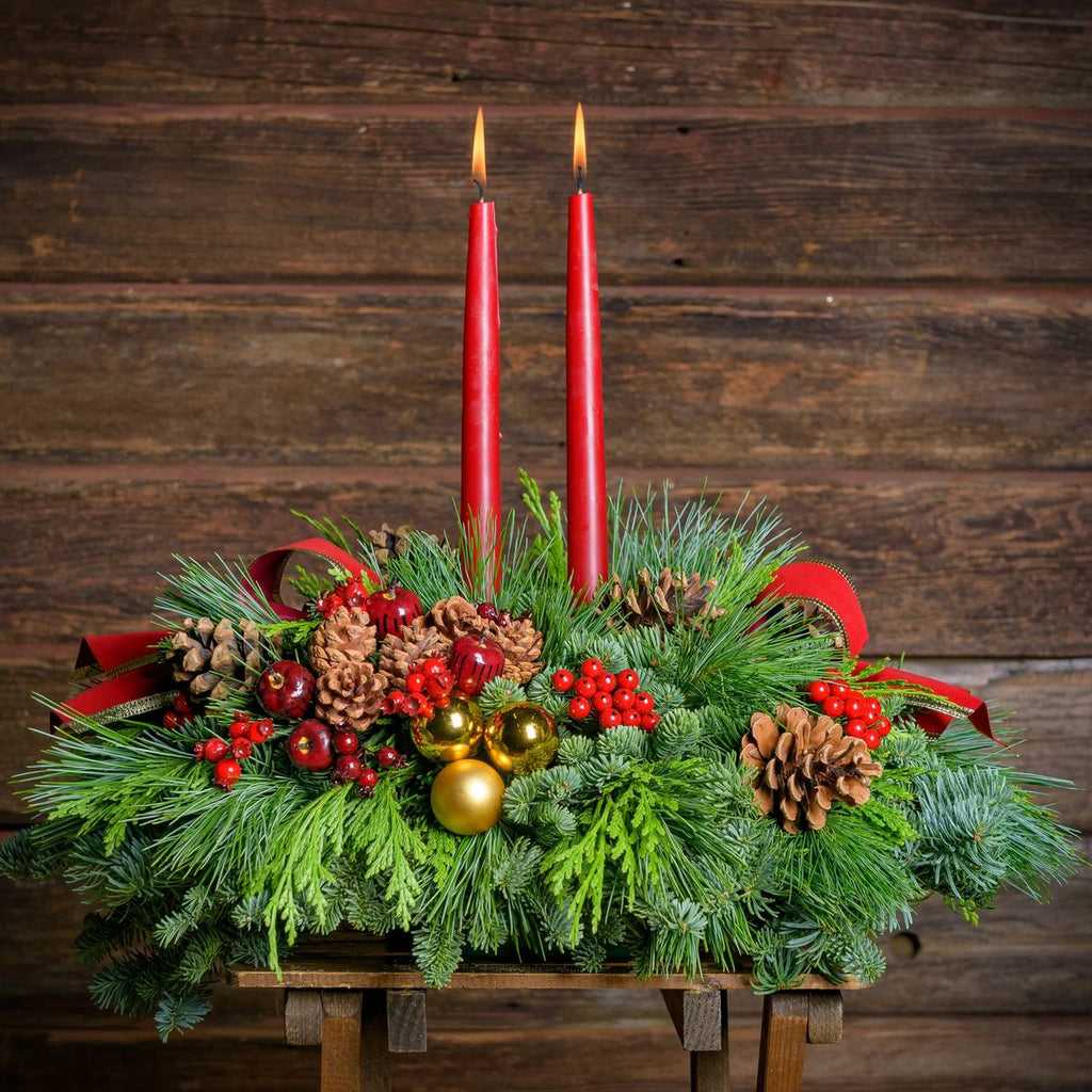 Decorative Christmas arrangement with red candles, pine cones, and berries on a wooden background